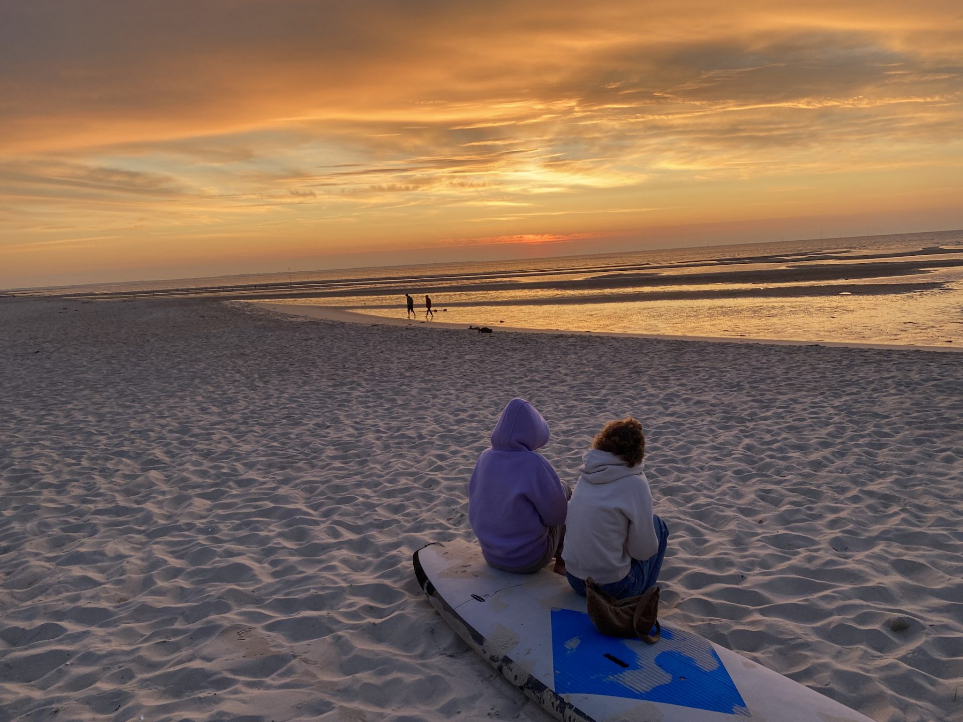 Schüler auf Surfbrett sitzend am Sylter Strand im Sonnenuntergang