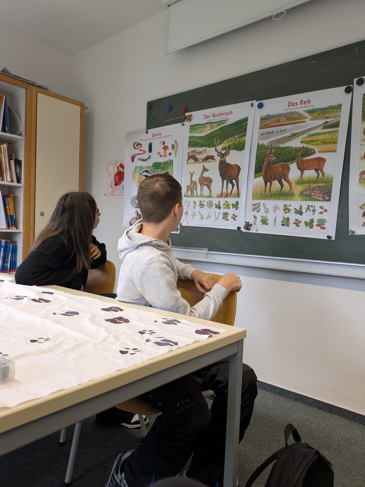 Ein Schüler und eine Schülerin vor Poster mit Tieren des Waldes